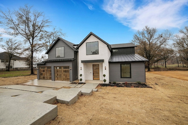 modern inspired farmhouse featuring an attached garage, driveway, metal roof, and a standing seam roof