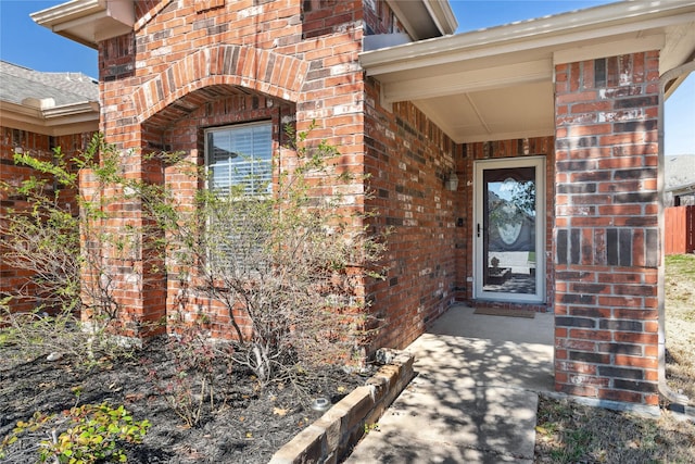 entrance to property featuring brick siding and roof with shingles