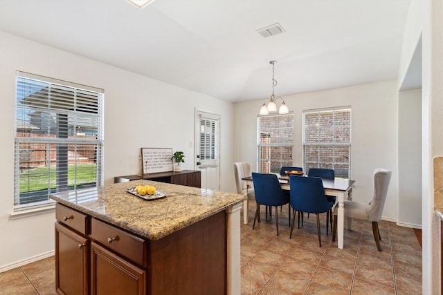 kitchen with decorative light fixtures, light stone countertops, baseboards, and a center island