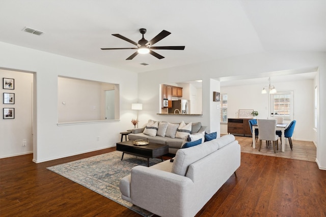 living area featuring dark wood finished floors, visible vents, ceiling fan with notable chandelier, and baseboards