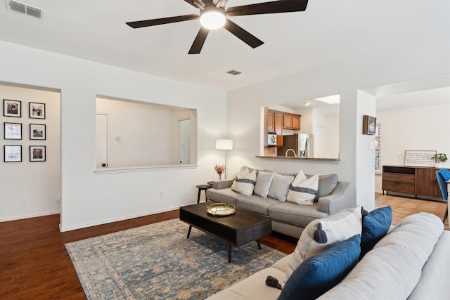 living room with baseboards, visible vents, dark wood-style flooring, and ceiling fan