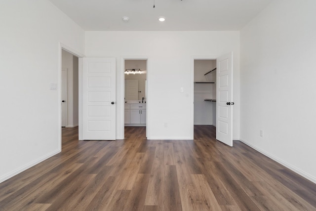 unfurnished bedroom featuring dark wood-style floors, connected bathroom, a closet, baseboards, and a spacious closet