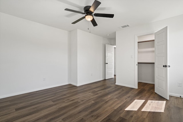 unfurnished bedroom with a ceiling fan, baseboards, visible vents, dark wood-type flooring, and a walk in closet