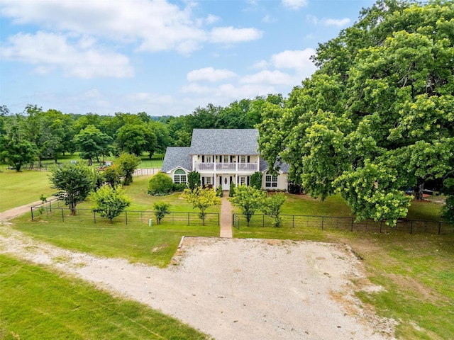 view of front of home with a rural view, a shingled roof, fence private yard, a front yard, and a balcony