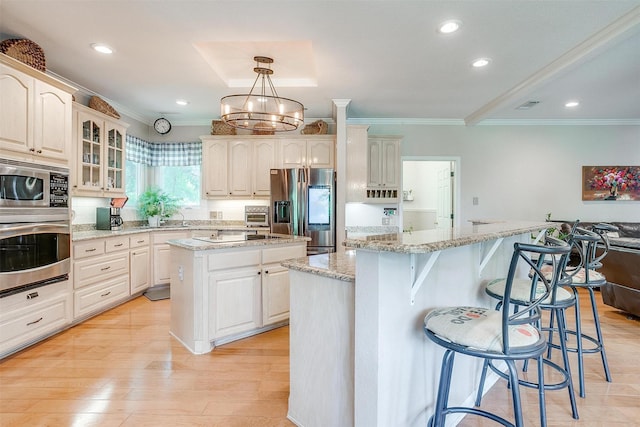 kitchen with a kitchen island, appliances with stainless steel finishes, a breakfast bar area, light wood finished floors, and glass insert cabinets