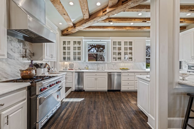 kitchen with backsplash, wall chimney range hood, beamed ceiling, light countertops, and appliances with stainless steel finishes