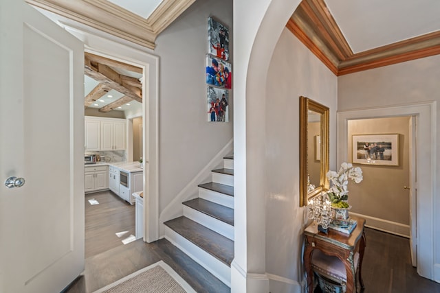 stairway featuring arched walkways, ornamental molding, baseboards, and wood finished floors