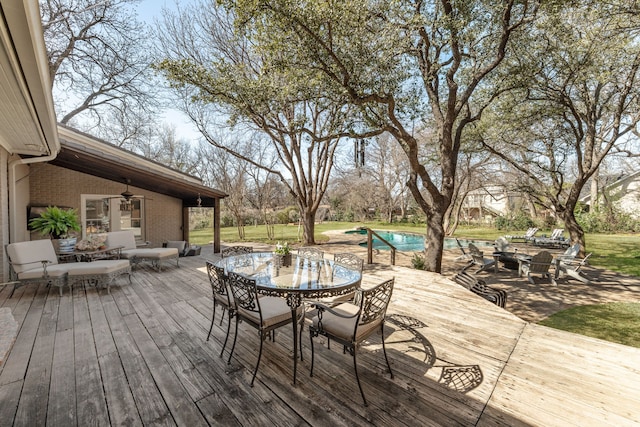 deck with an outdoor pool, outdoor dining area, a fire pit, and ceiling fan