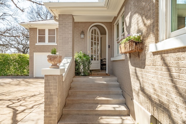 doorway to property with brick siding, driveway, and a garage