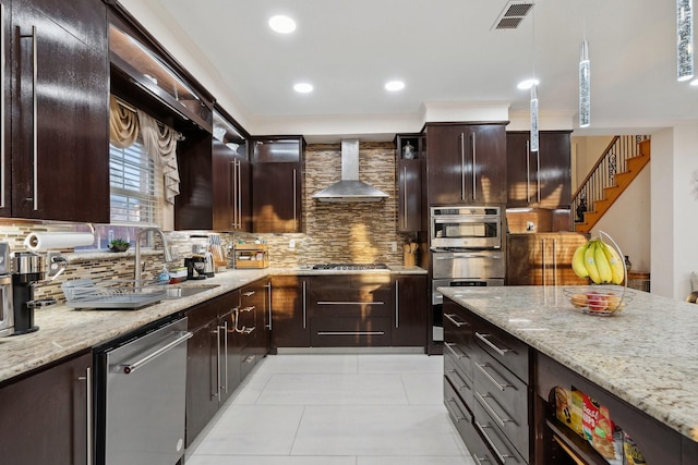 kitchen with a sink, light stone counters, backsplash, stainless steel appliances, and wall chimney range hood