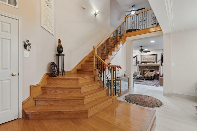 stairs with visible vents, baseboards, a warm lit fireplace, a high ceiling, and a ceiling fan