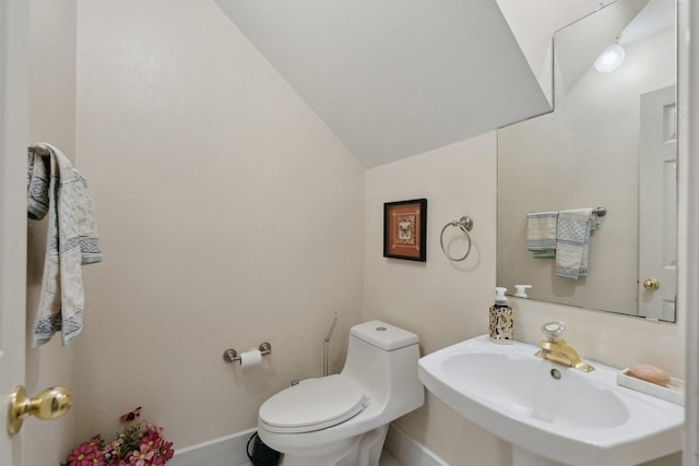 half bathroom with vaulted ceiling, toilet, baseboards, and a sink