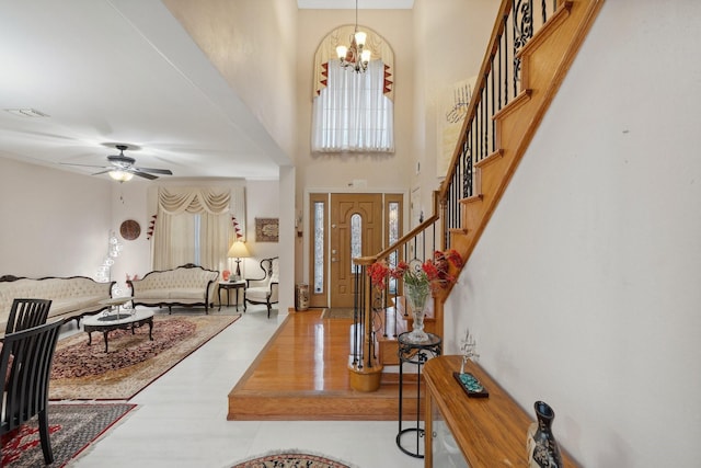 entrance foyer with visible vents, stairway, ceiling fan with notable chandelier, a towering ceiling, and wood finished floors