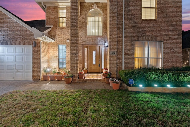 doorway to property featuring brick siding, an attached garage, and a lawn