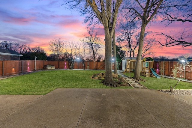 yard at dusk with a patio, a fenced backyard, an outdoor structure, a storage unit, and a playground