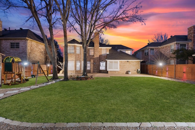 back of property at dusk with fence, a lawn, a playground, a patio area, and brick siding