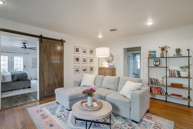 living room featuring visible vents, crown molding, a barn door, and wood finished floors