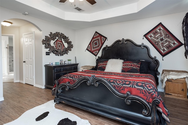 bedroom featuring baseboards, a raised ceiling, arched walkways, and wood finished floors