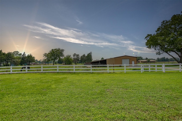 view of yard featuring a rural view, fence, a garage, a pole building, and an outbuilding