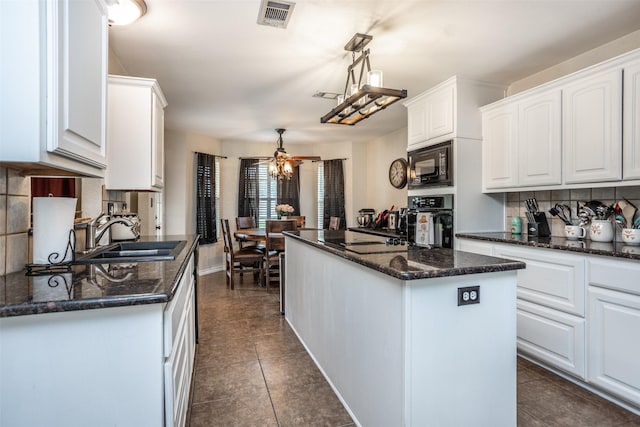 kitchen with visible vents, black appliances, a sink, a kitchen island, and white cabinets