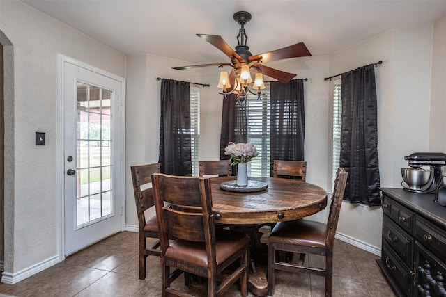 dining space featuring dark tile patterned flooring, arched walkways, baseboards, and ceiling fan