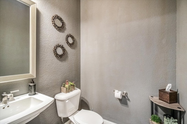 half bath featuring toilet, a textured wall, and a sink