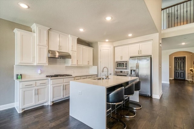 kitchen with a sink, under cabinet range hood, white cabinetry, arched walkways, and appliances with stainless steel finishes