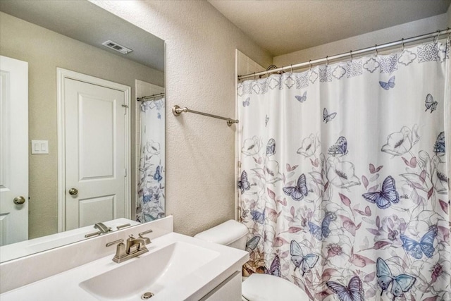 bathroom featuring vanity, a shower with shower curtain, visible vents, toilet, and a textured wall