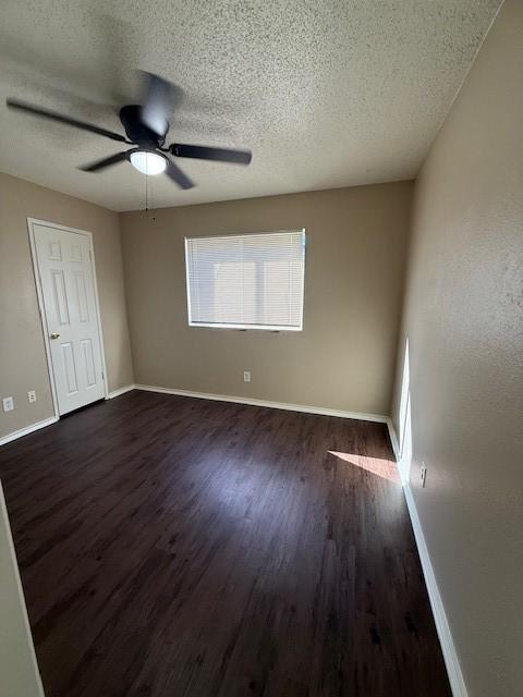 spare room featuring dark wood finished floors, a textured ceiling, baseboards, and a ceiling fan