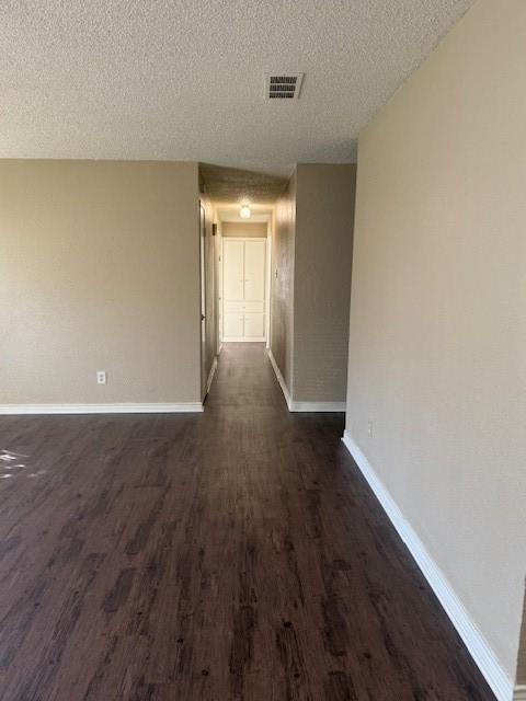 hall with visible vents, baseboards, a textured ceiling, and dark wood finished floors