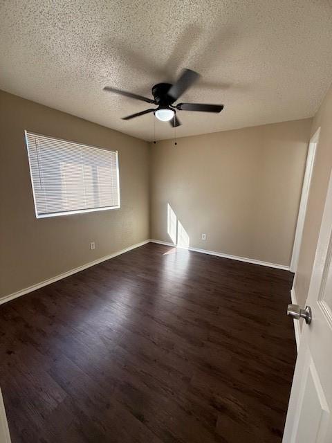 empty room featuring ceiling fan, baseboards, a textured ceiling, and dark wood-style floors