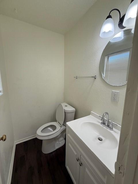 half bath with vanity, toilet, wood finished floors, and baseboards