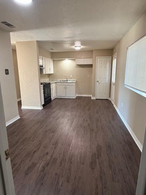 kitchen featuring visible vents, dark wood-type flooring, baseboards, white cabinetry, and black / electric stove