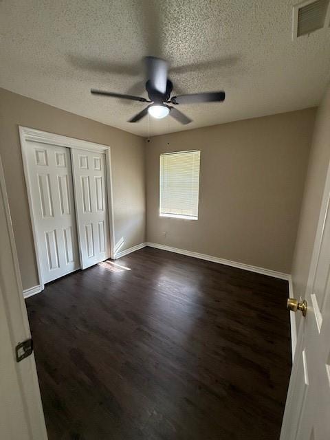 unfurnished bedroom with visible vents, a ceiling fan, dark wood finished floors, a closet, and baseboards