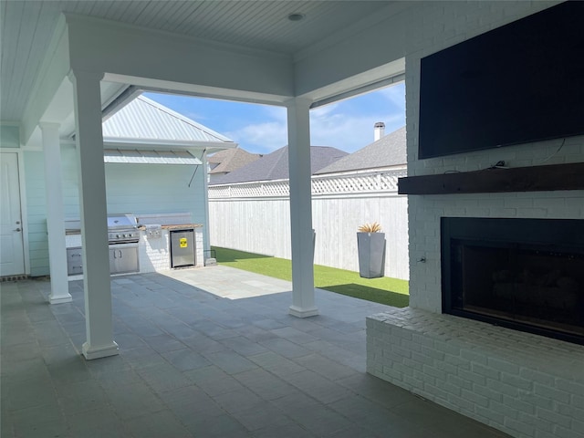 view of patio with grilling area, an outdoor brick fireplace, fence, and exterior kitchen
