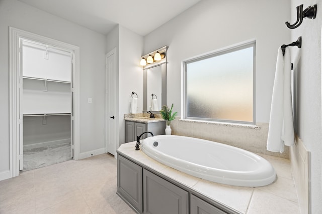 bathroom featuring a spacious closet, tile patterned floors, baseboards, a bath, and vanity