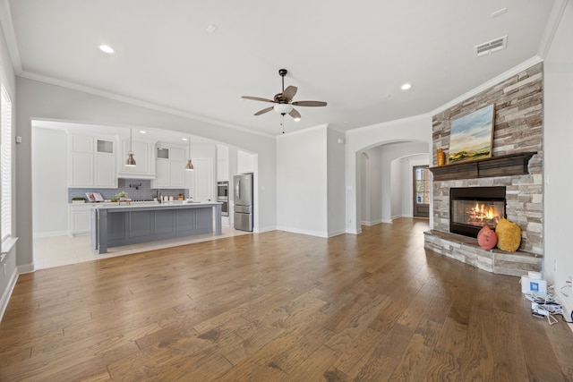 unfurnished living room featuring visible vents, light wood-style floors, a stone fireplace, baseboards, and ceiling fan