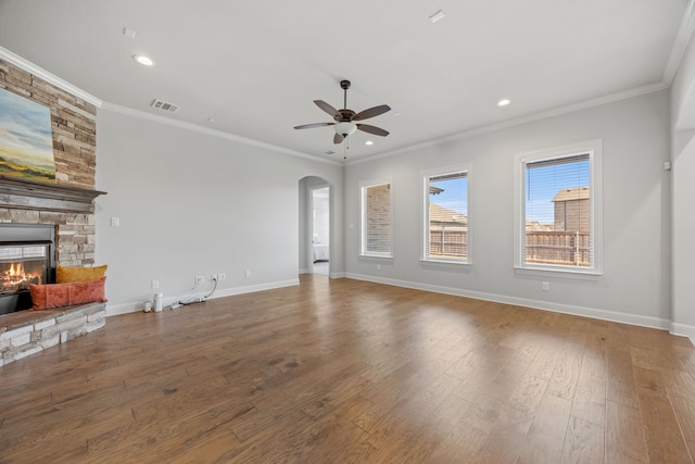 unfurnished living room featuring wood finished floors, arched walkways, a fireplace, crown molding, and baseboards