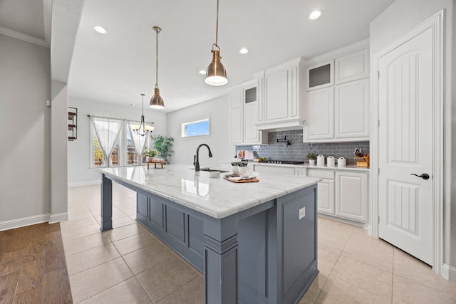 kitchen with an island with sink, a sink, glass insert cabinets, white cabinetry, and backsplash