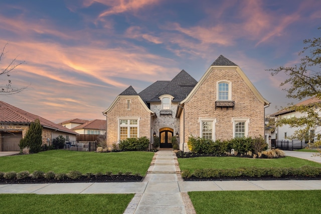 french country home with a front lawn, fence, and brick siding