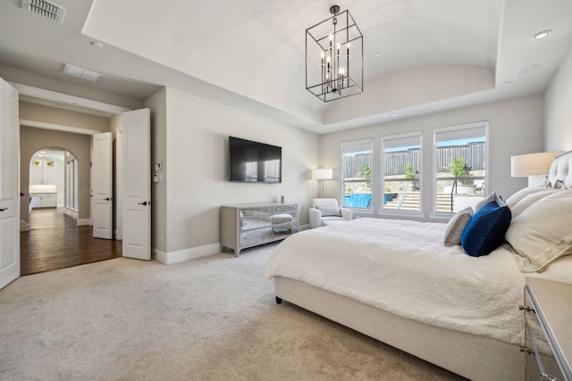 carpeted bedroom with visible vents, baseboards, an inviting chandelier, arched walkways, and a raised ceiling