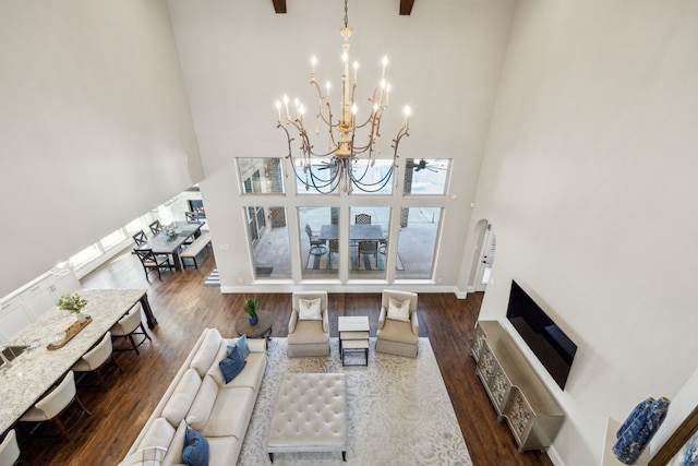 living area with a notable chandelier, wood finished floors, baseboards, and a towering ceiling