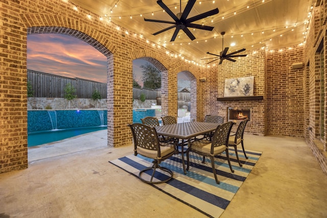 view of patio featuring ceiling fan, a fenced backyard, outdoor dining space, and an outdoor brick fireplace