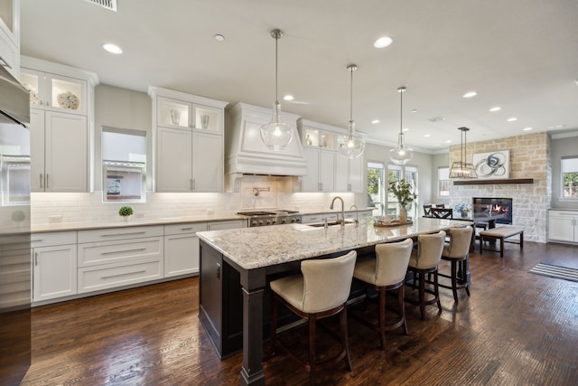 kitchen with a sink, decorative backsplash, a stone fireplace, custom range hood, and white cabinets