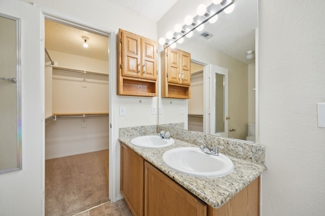 bathroom with a sink, visible vents, a textured ceiling, and a spacious closet