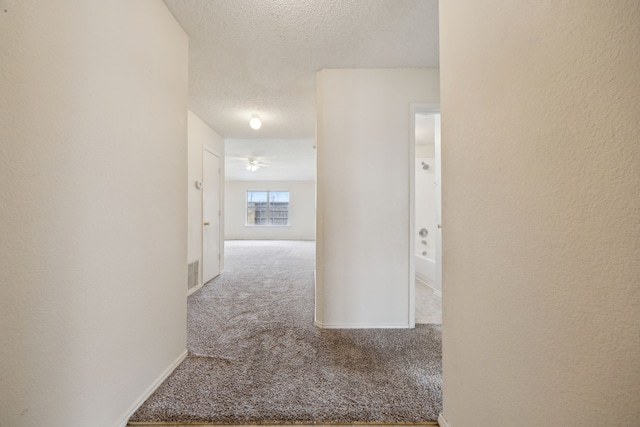 corridor with visible vents, baseboards, carpet, a textured wall, and a textured ceiling