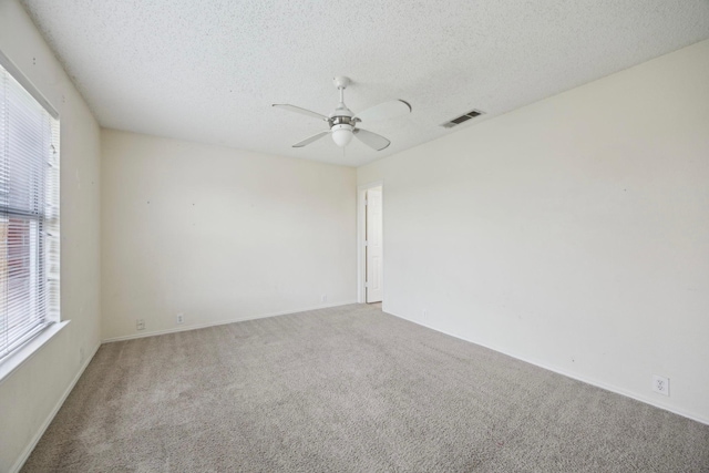 carpeted empty room featuring baseboards, a ceiling fan, visible vents, and a textured ceiling