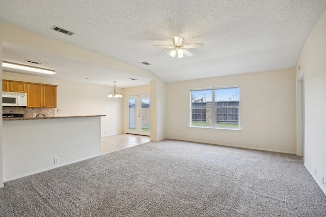 unfurnished living room featuring a textured ceiling, ceiling fan with notable chandelier, visible vents, and light carpet