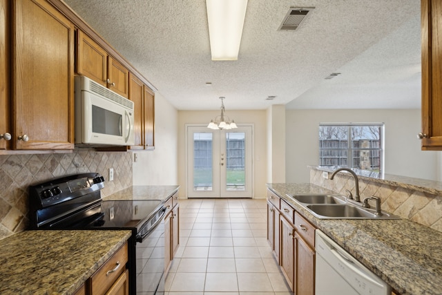 kitchen featuring visible vents, brown cabinets, a sink, tasteful backsplash, and white appliances