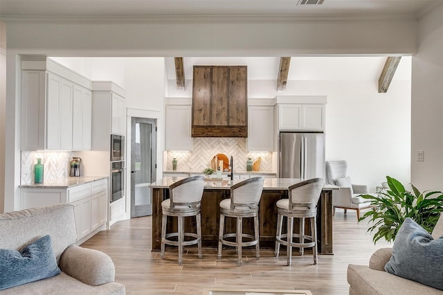 kitchen featuring beamed ceiling, light stone countertops, open floor plan, and stainless steel appliances